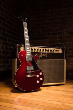 a red electric guitar sitting on top of a hard wood floor next to an amp