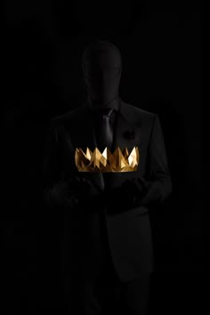 a man in a tuxedo with gold crowns on his head and hands behind him