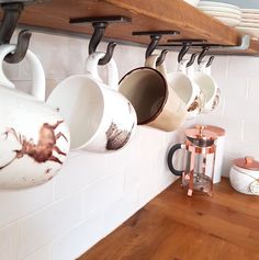 coffee mugs are hanging on the wall in a kitchen with wooden counter tops and shelves