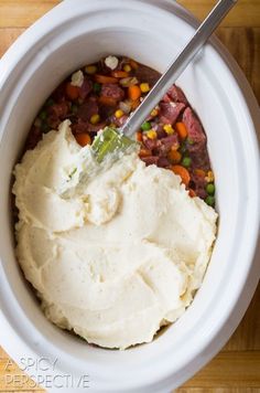 a bowl filled with mashed potatoes, meat and veggies on top of a wooden table