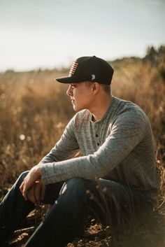 a man sitting in the middle of a field wearing a black hat and grey shirt