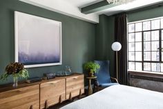 a bedroom with green walls and white bedding, two blue chairs and a painting on the wall