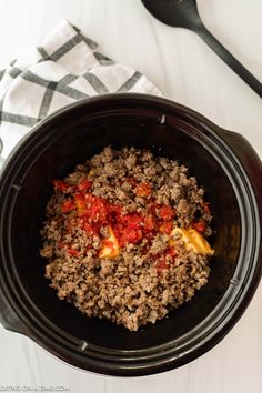 a black crock pot filled with ground beef and tomato sauce next to a spoon