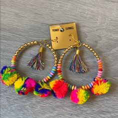 two pairs of colorful pom poms hanging from hoop earrings on a wooden surface