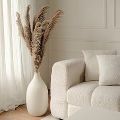 a white couch sitting next to a tall vase filled with dry grass on top of a hard wood floor