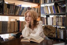 a woman sitting at a table in front of a bookshelf with an open book