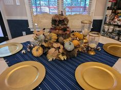 the table is set with gold plates and pumpkins