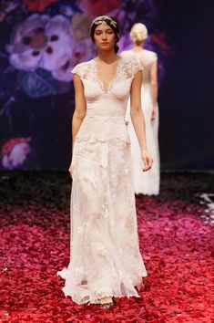 a woman walking down a runway wearing a white dress with flowers on the skirt and headpiece