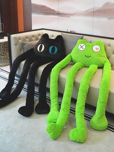 two stuffed animals sitting on a couch in front of a large spider and black cat