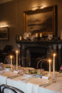 the table is set with place settings and candles in front of an old fire place