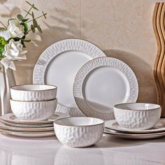 a white dinner set on a table with flowers in the vase and plates around it