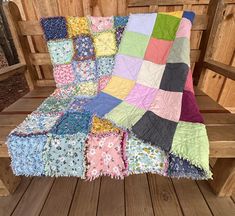 a multicolored quilt sitting on top of a wooden bench next to a fence