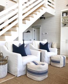 a living room with white couches and blue pillows on the bottom floor next to a stair case