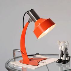 an orange desk lamp sitting on top of a glass table next to a figurine