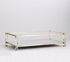 a glass and brass coffee table with two shelves on each side, against a white background