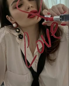 a woman with red lipstick is holding up the word love to her face while wearing a white shirt and black tie