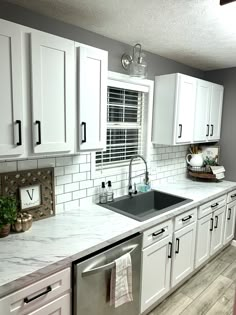 a kitchen with white cabinets and marble counter tops is pictured in this image, there are towels hanging on the dishwasher