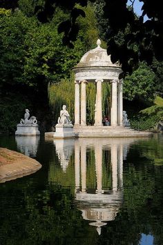 a gazebo sitting in the middle of a pond surrounded by trees and water with statues around it