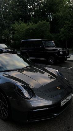 two cars parked in a lot next to each other with trees and bushes behind them