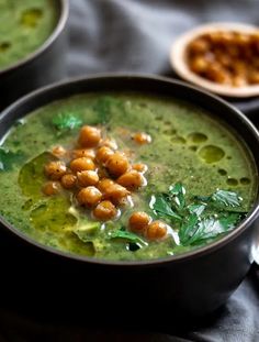 two bowls filled with green soup and garnished with chickpeas