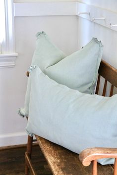 two light blue pillows sitting on top of a wooden bench in front of a window