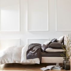 a bed with pillows and blankets on top of it in front of a white wall