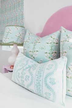 a bed with blue and white pillows on it's headboard next to a pink chair