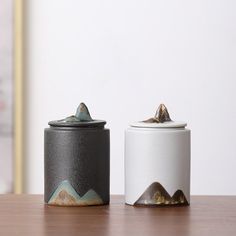 two black and white canisters sitting on top of a wooden table next to each other