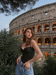 a beautiful young woman standing in front of an old roman collise at sunset