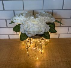 white flowers in a glass jar with fairy lights on the table next to a brick wall