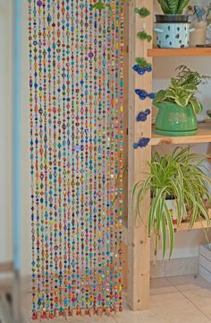 a wooden shelf filled with lots of plants next to a wall covered in colorful beads