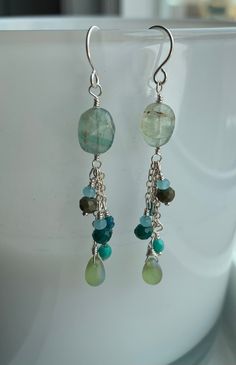 earrings with green and blue beads hanging from them on a white cup in front of a window