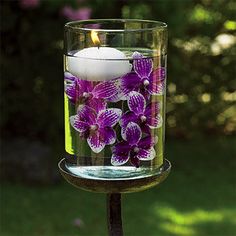 a candle that is sitting in a glass vase with purple flowers on the outside and inside