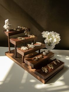 three wooden trays with jewelry on them and flowers in a vase next to them