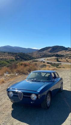 an old blue car parked on the side of a dirt road