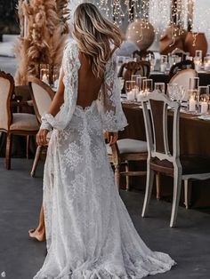 a woman standing in front of a table wearing a white dress with long sleeves and open back