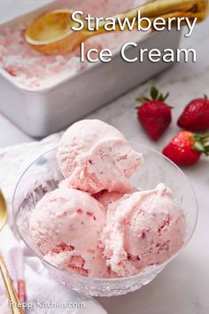 three scoops of strawberry ice cream in a glass bowl with strawberries on the side