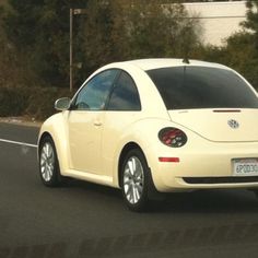 a white vw bug driving down the road in front of some trees and bushes