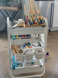 a white cart filled with lots of crafting supplies on top of a hard wood floor