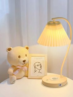 a teddy bear sitting on top of a table next to a lamp and picture frame