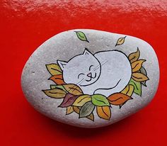 a painted rock with a white cat sleeping on it's back and leaves around its neck