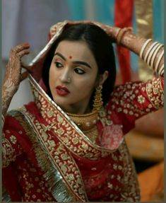 a woman in a red and gold bridal outfit with her hands on her head