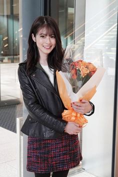 a woman in a black leather jacket holding a bouquet of flowers and posing for the camera