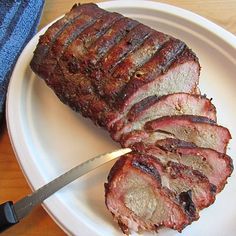 a white plate topped with sliced up meat next to a knife and fork on top of a wooden table