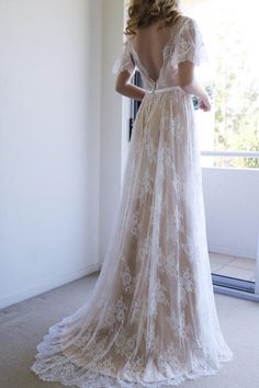 a woman in a wedding dress standing by a window looking out the window with her back to the camera