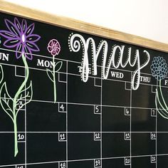 a calendar with flowers drawn on it and the word may written in white chalk next to a wooden frame