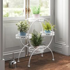 three tiered plant stand with potted plants in front of a window, on wooden floor