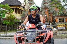 two people riding on the back of an orange four - wheeler with green helmet and goggles