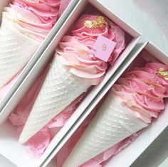 two ice cream cones with pink icing and gold decorations in a white paper box