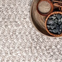 two bowls filled with rocks on top of a white rug next to bamboo spoons